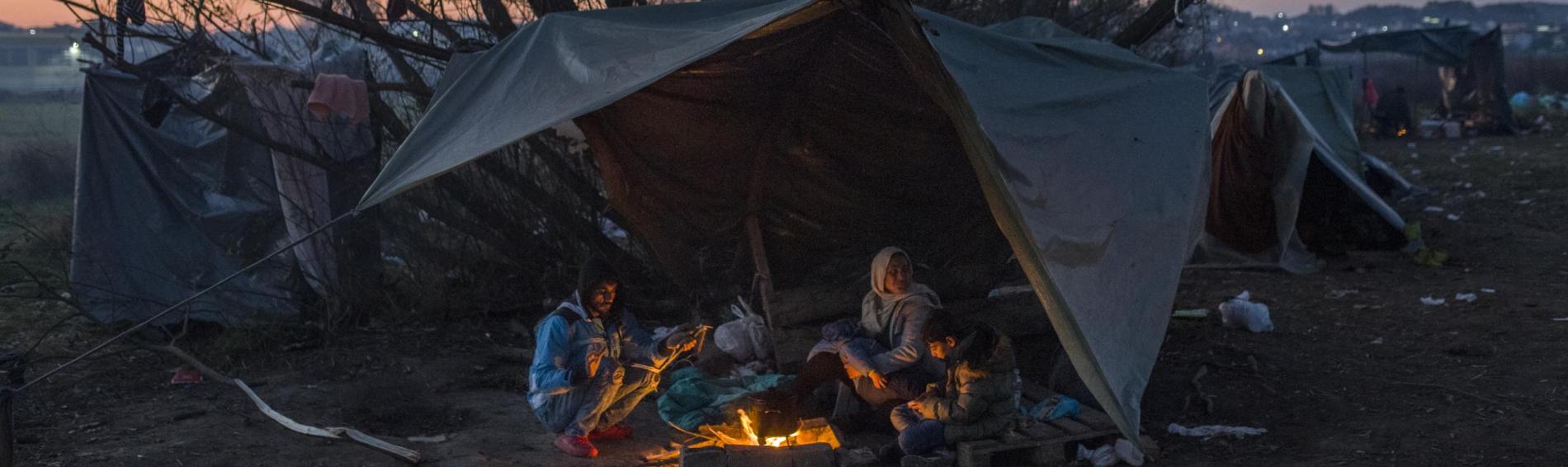 familie zit rond een vuurtje onder een zeil in de koude bij zonsopgang
