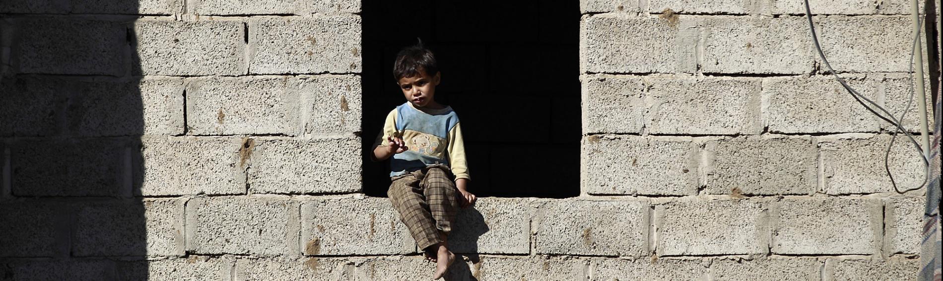 Un petit garçon à la fenêtre d'un bâtiment en ruines.