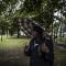 Een Afrikaanse man schuilt onder een geruite paraplu voor de regen, ergens in een Brussels park.